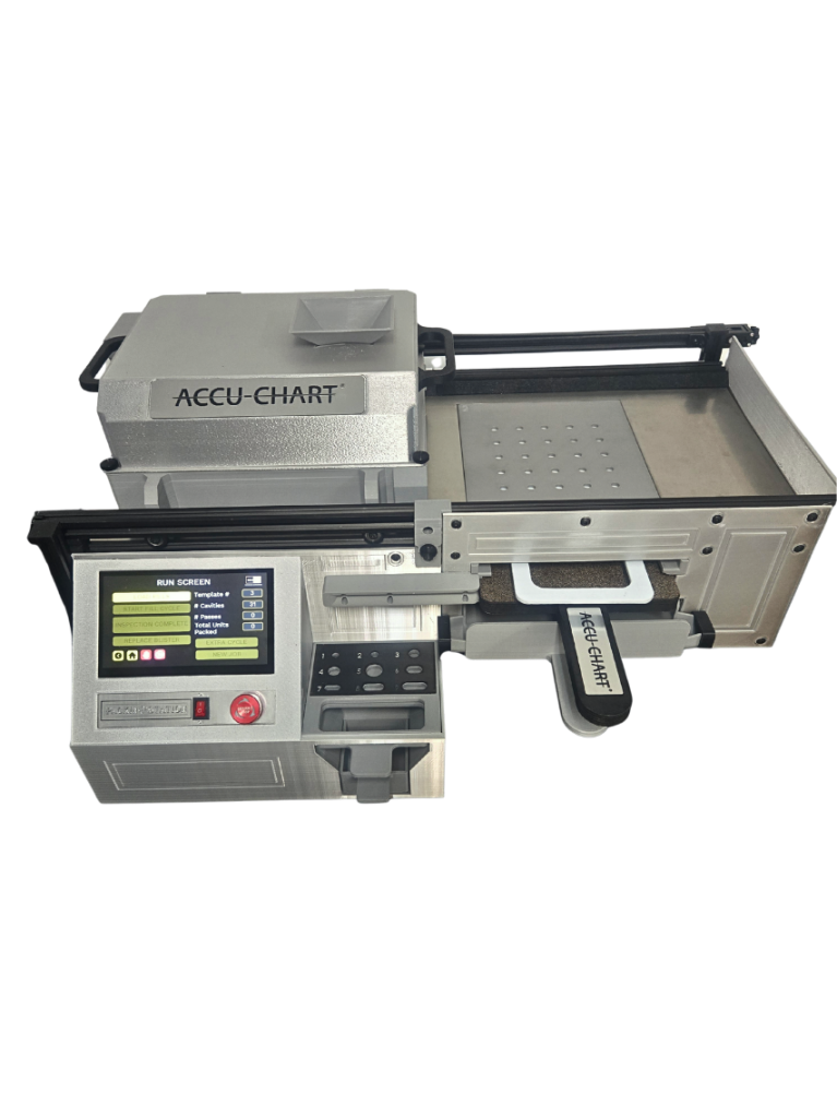 A silver Accu-Chart machine with a digital control panel, display screen, buttons, and a tray. The device appears to be used for dispensing or packaging medication.